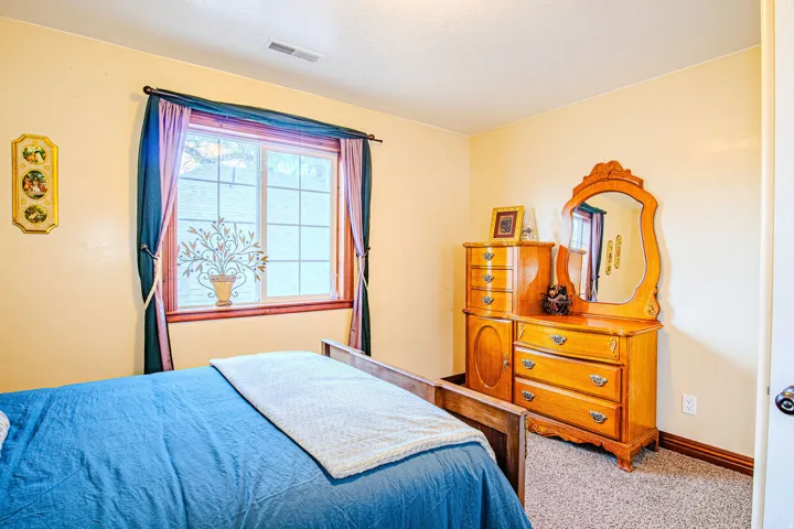 Carpeted third bedroom featuring a window with wood trim and a baseboard heating vent