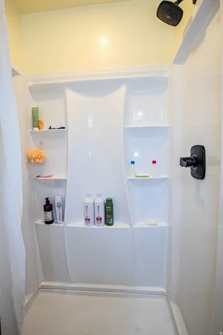 White shower enclosure featuring built-in shelving, matte black fixtures, and a shower curtain rod