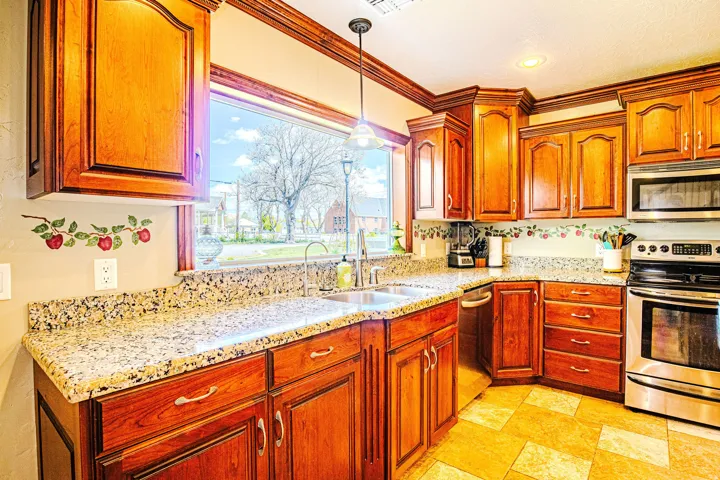 Kitchen featuring an undermount double-basin sink, stainless steel appliances, abundant wood cabinetry with crown molding, granite countertops, and tiled flooring