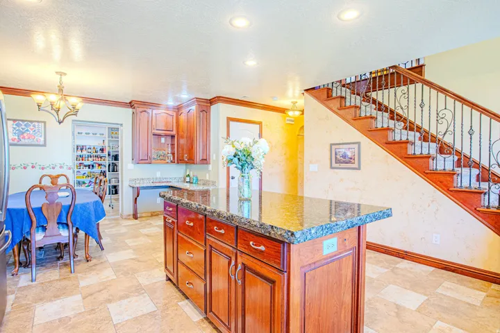 Kitchen featuring a central island with a granite countertop, wood cabinetry, and recessed lighting. Stairs to second floor
