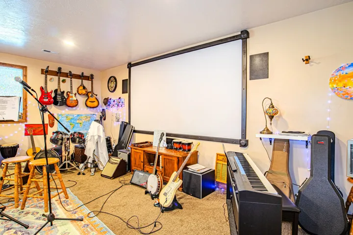Carpeted room featuring a large wall-mounted projector screen, built-in wall speakers, and a window with wood trim