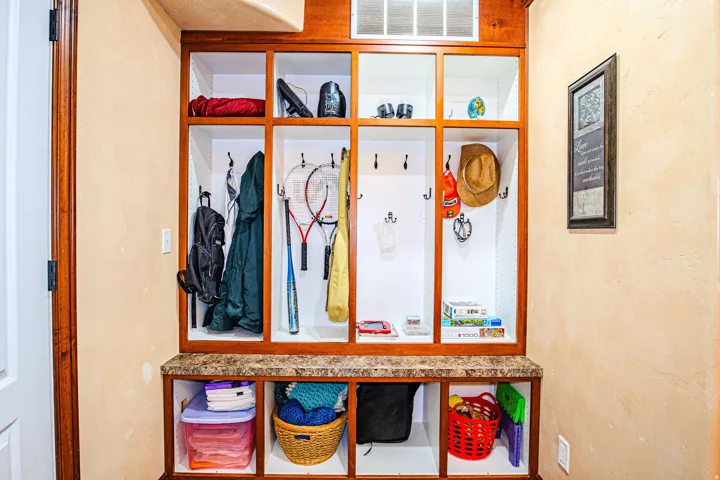 Built-i  organization system featuring wood-finish framing, integrated seating with a stone-finish countertop, upper and lower storage cubbies, and multiple coat hooks