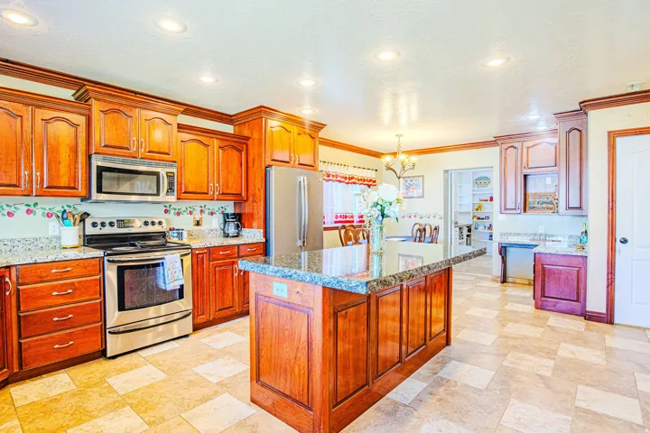 Kitchen featuring a central island with an extended countertop, wood cabinetry, granite countertops, and stainless steel appliances