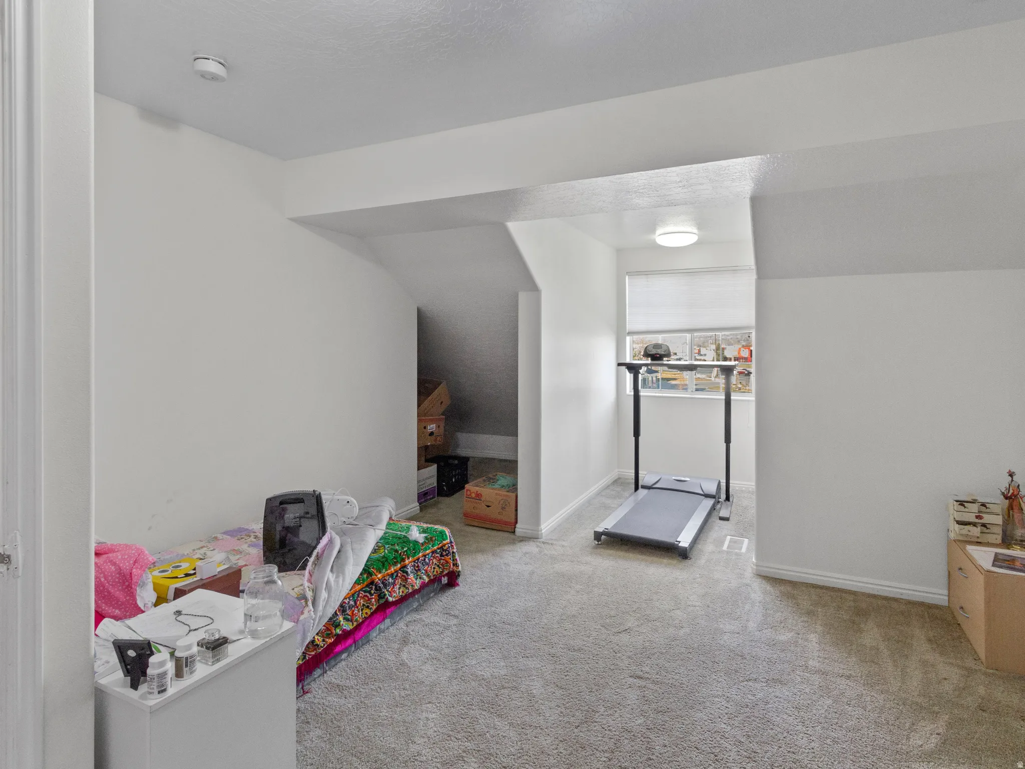 Carpeted attic space featuring sloped ceilings, a window with a roller shade, and white baseboards