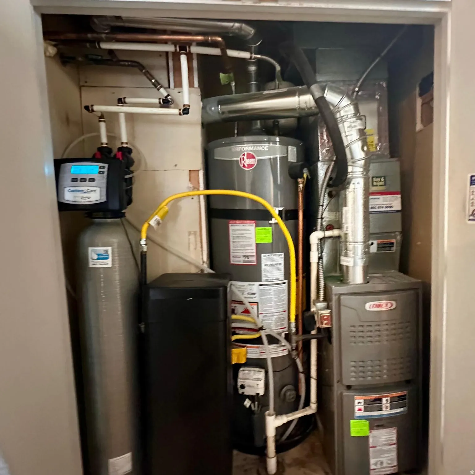Utility closet featuring a water heater, furnace, water softener system, and associated copper and PVC plumbing