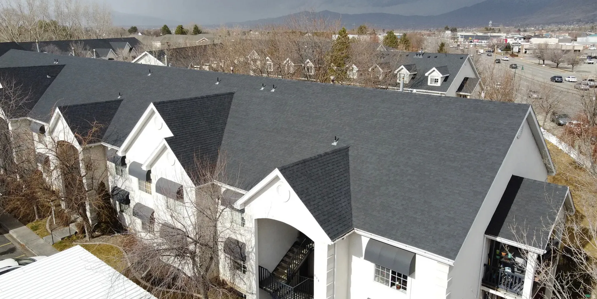 Multi-level residential building featuring a dark shingle roof, light-toned exterior siding, and multiple dormer windows