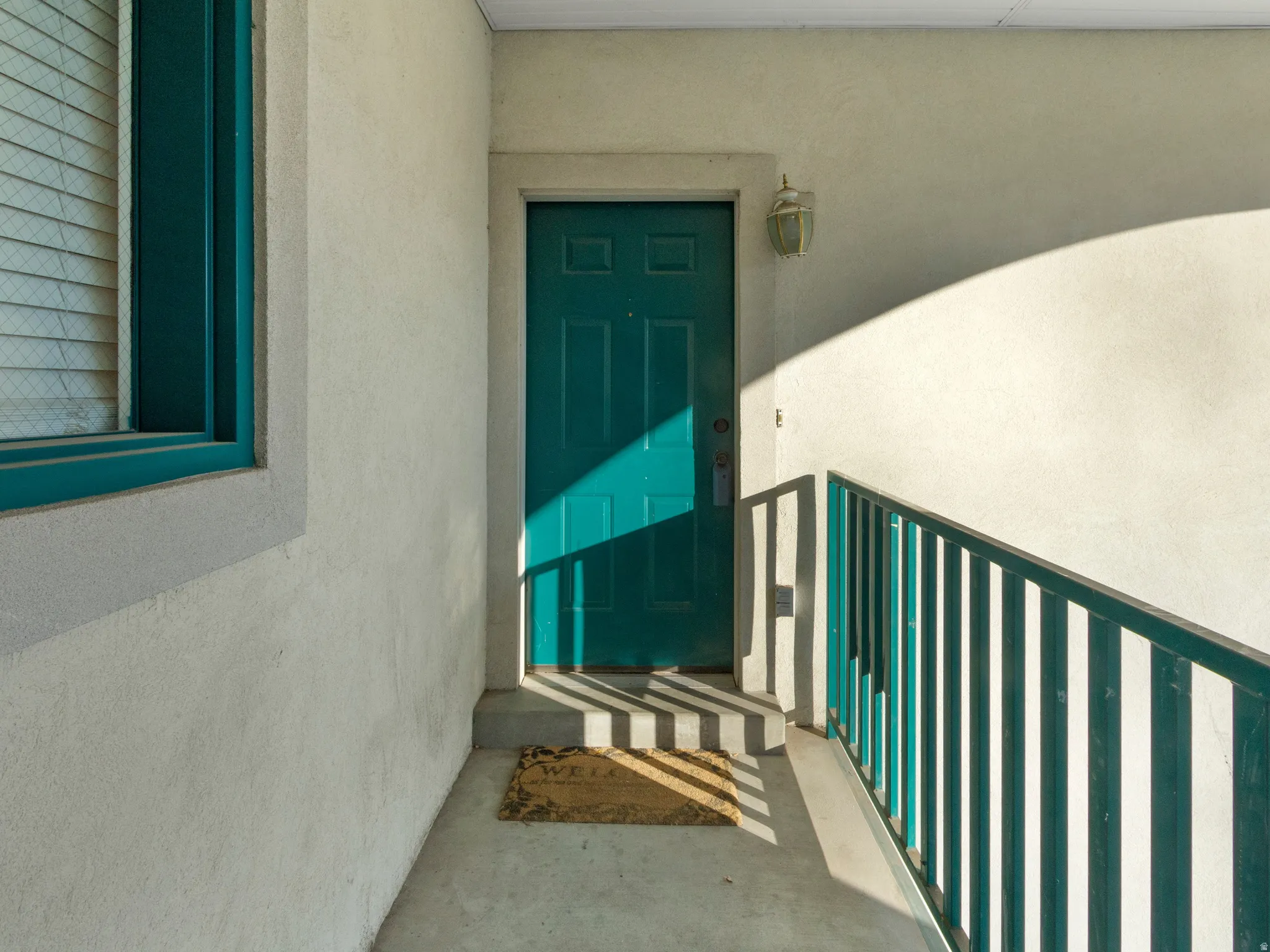 Entryway featuring a teal door, exterior wall sconce, and a teal-painted metal railing