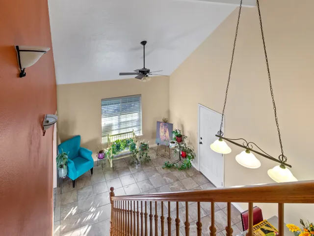 Foyer featuring vaulted ceilings, tile flooring, a multi-light chandelier, a ceiling fan, and a solid wood handrail with balusters