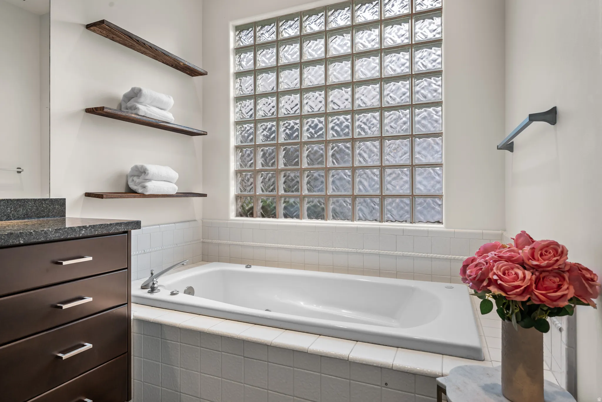 Deep soaking tub with chrome fixtures, surrounded by white tile and a prominent glass block window