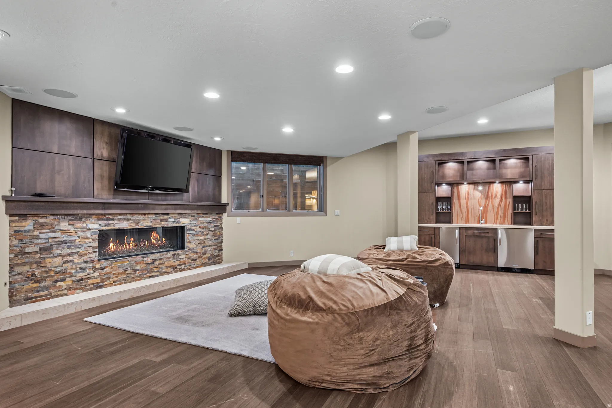 Spacious room featuring wood-finish flooring, recessed lighting, and a stone-clad fireplace with a built-in television