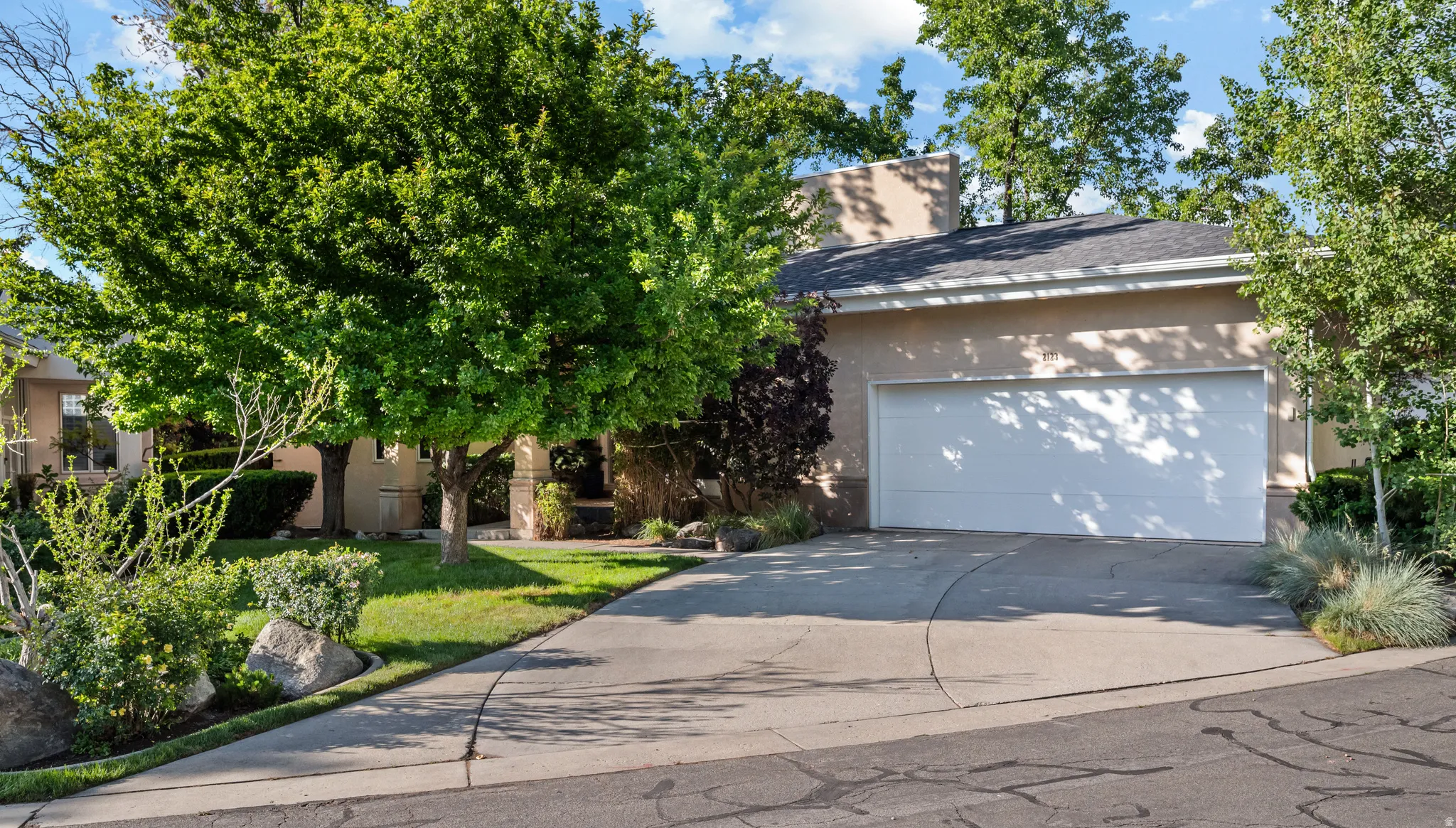 Stucco exterior with a two-car garage, concrete driveway, and mature landscaping