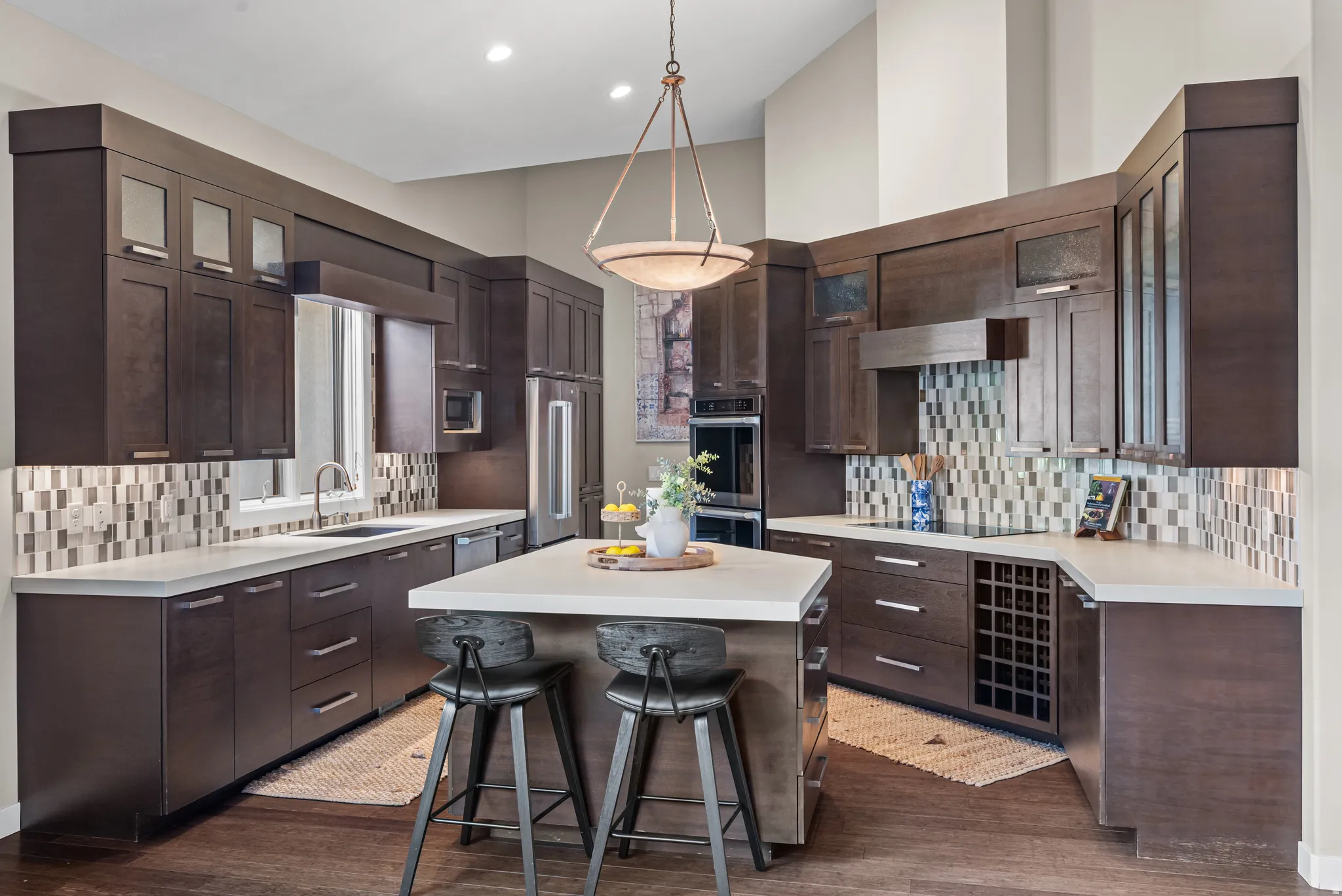 Custom kitchen featuring rich wood-finish cabinetry, a central island with countertop seating, stainless-steel appliances, a tiled backsplash, and recessed and pendant lighting