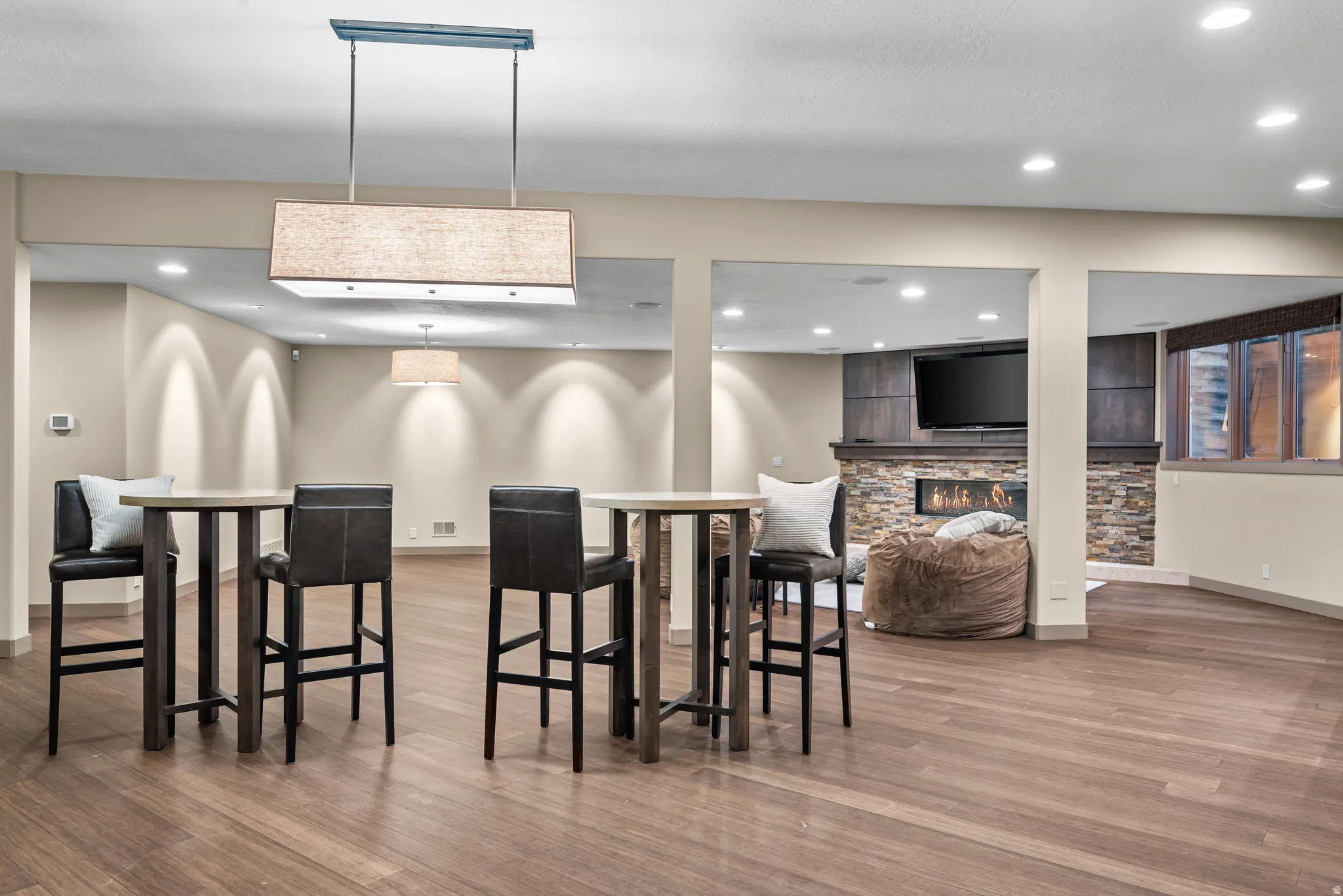 Spacious recreation room featuring wood-finish flooring, recessed lighting, and a linear chandelier