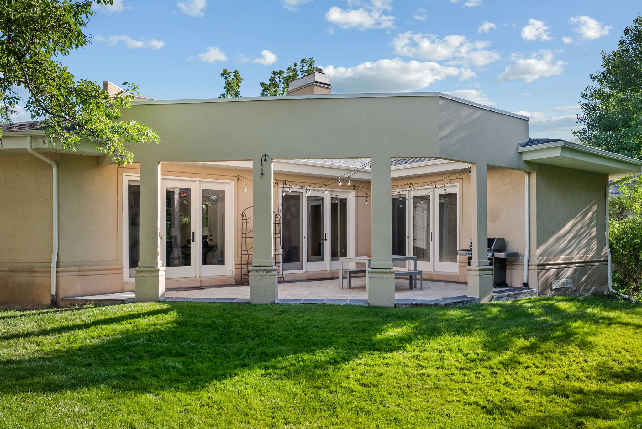 Rear exterior featuring a covered patio with architectural columns, multiple sets of glass French doors, and a stone-look paver patio