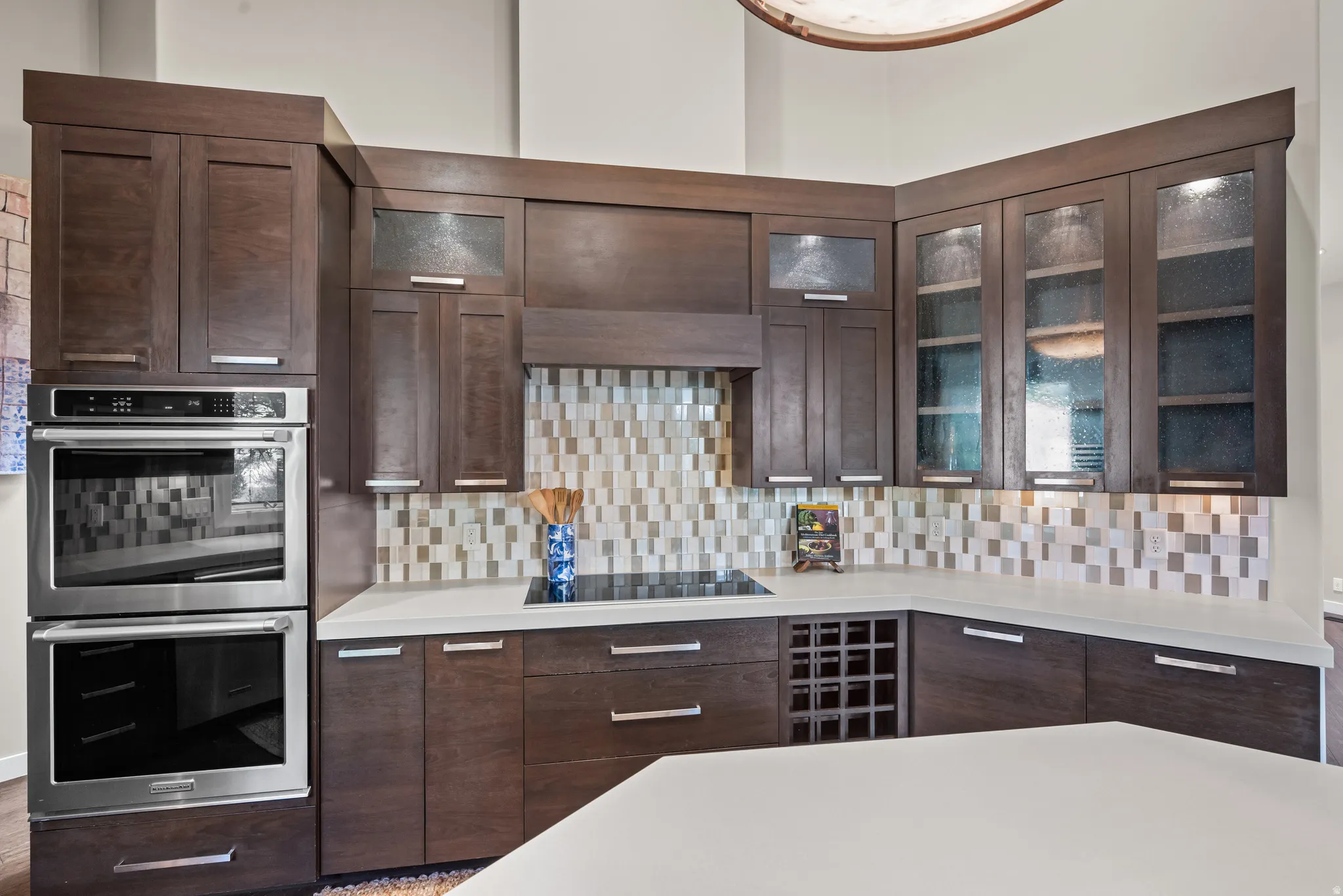 Contemporary kitchen featuring dark wood-finish cabinetry, integrated double wall ovens, and a mosaic tile backsplash