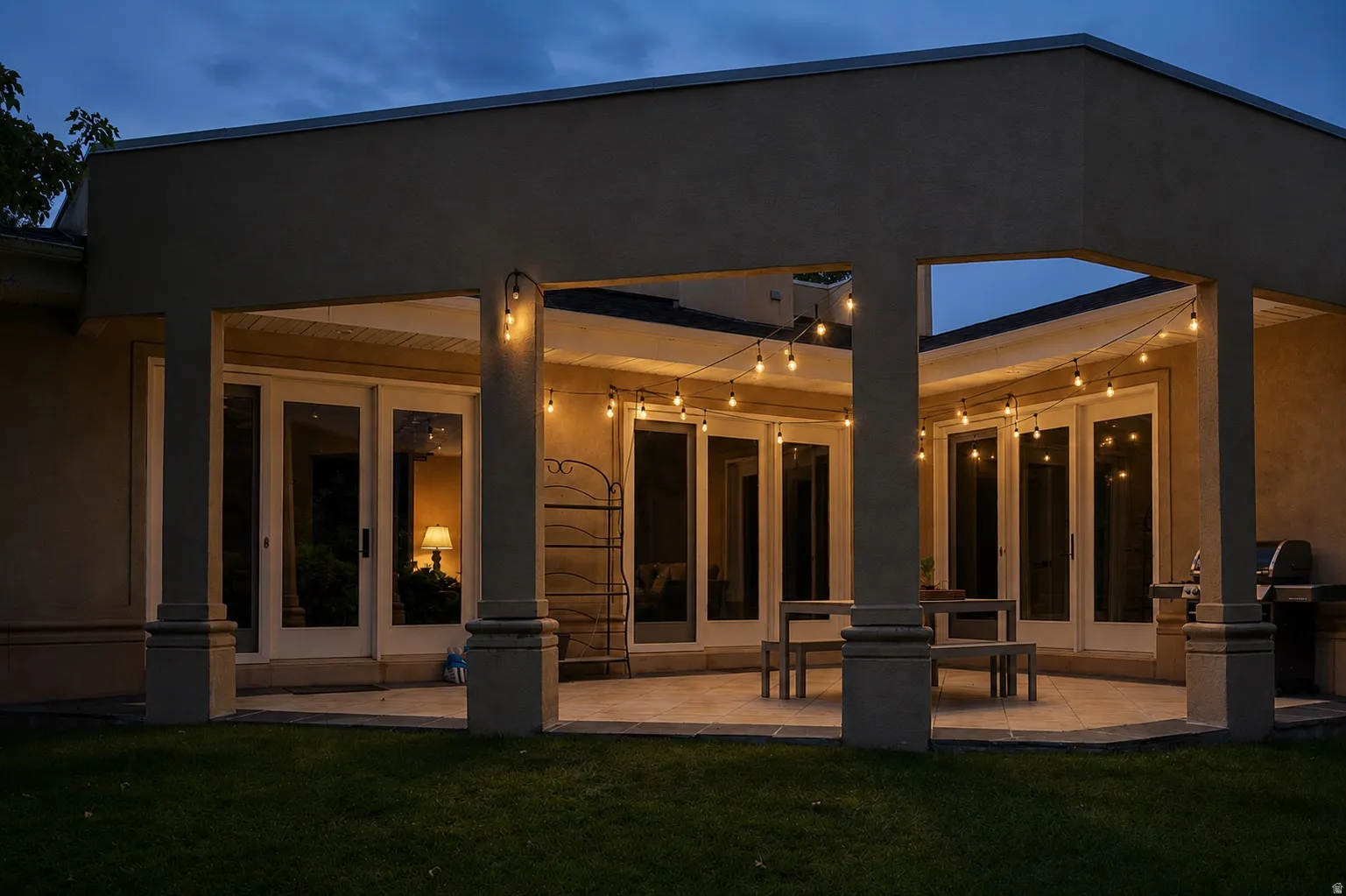 Covered patio with string lighting, multiple sets of French doors, an expansive concrete patio, and a manicured lawn