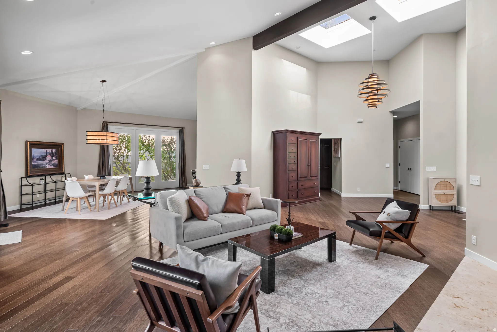 Expansive living area featuring high vaulted ceilings, multiple skylights, exposed beam accents, and wood-finish flooring