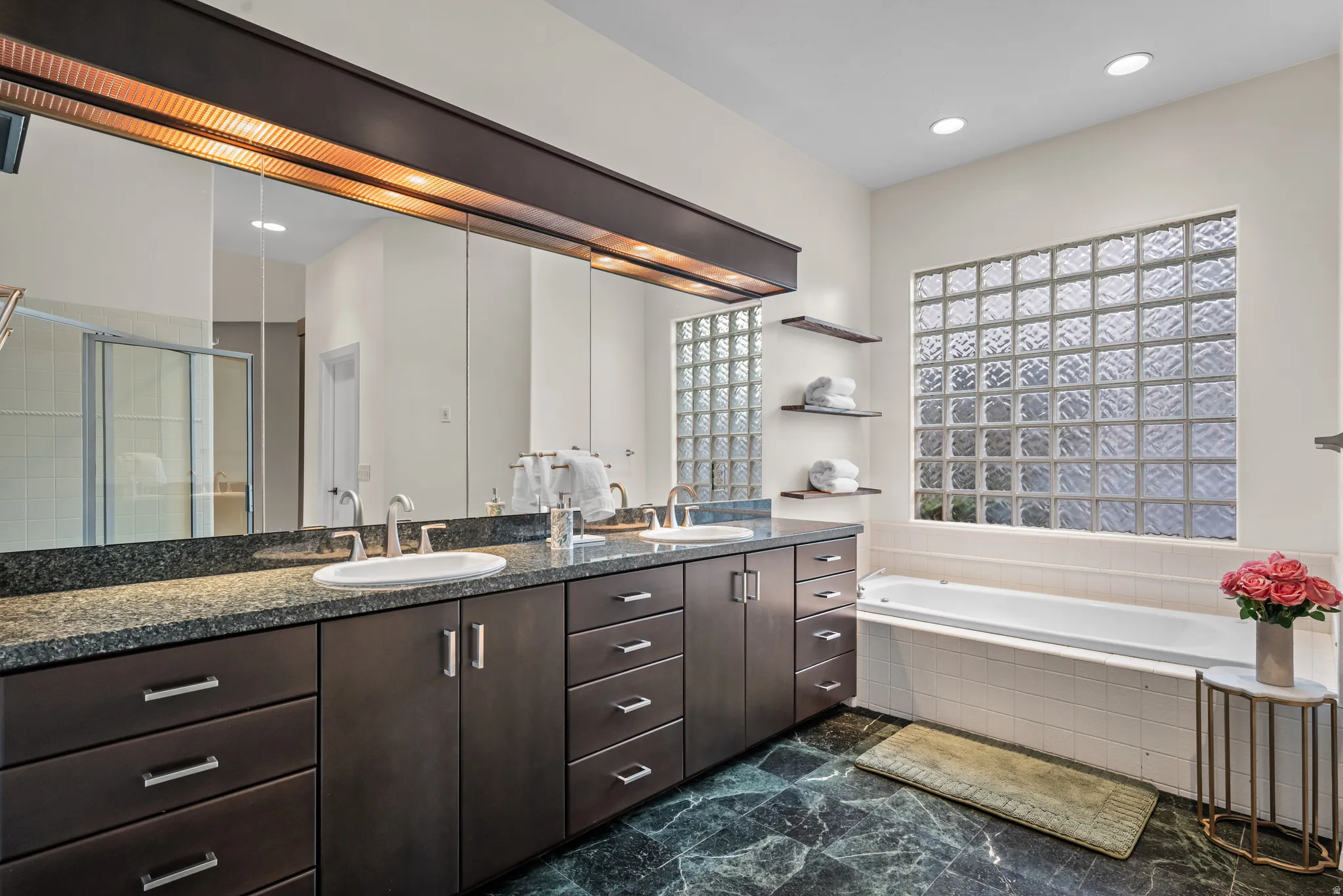Bathroom featuring a dual vanity with undermount sinks, stone countertops, and extensive dark wood-finish cabinetry