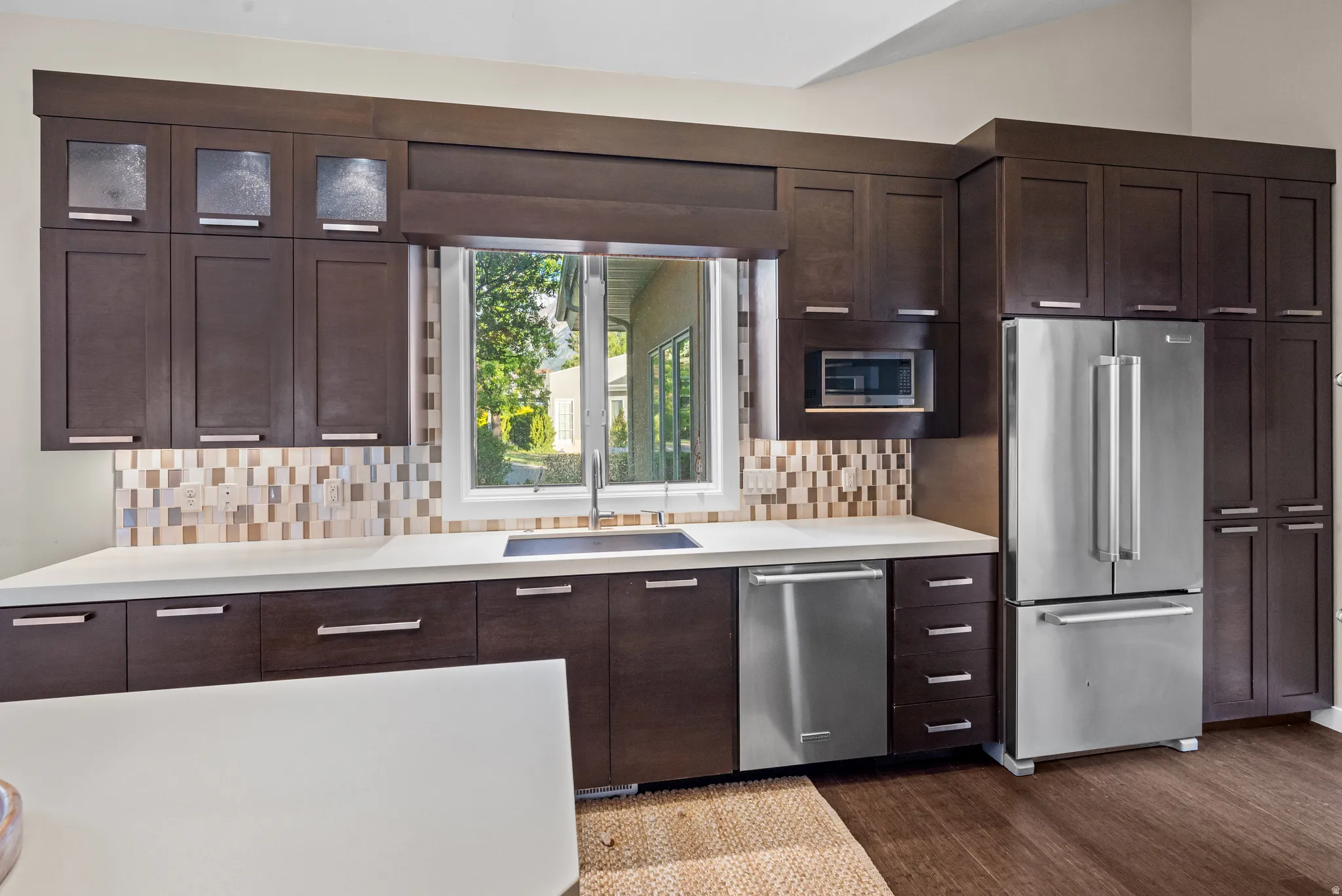 Kitchen featuring dark wood-finish cabinetry, stainless steel appliances, a tile backsplash, and light countertops