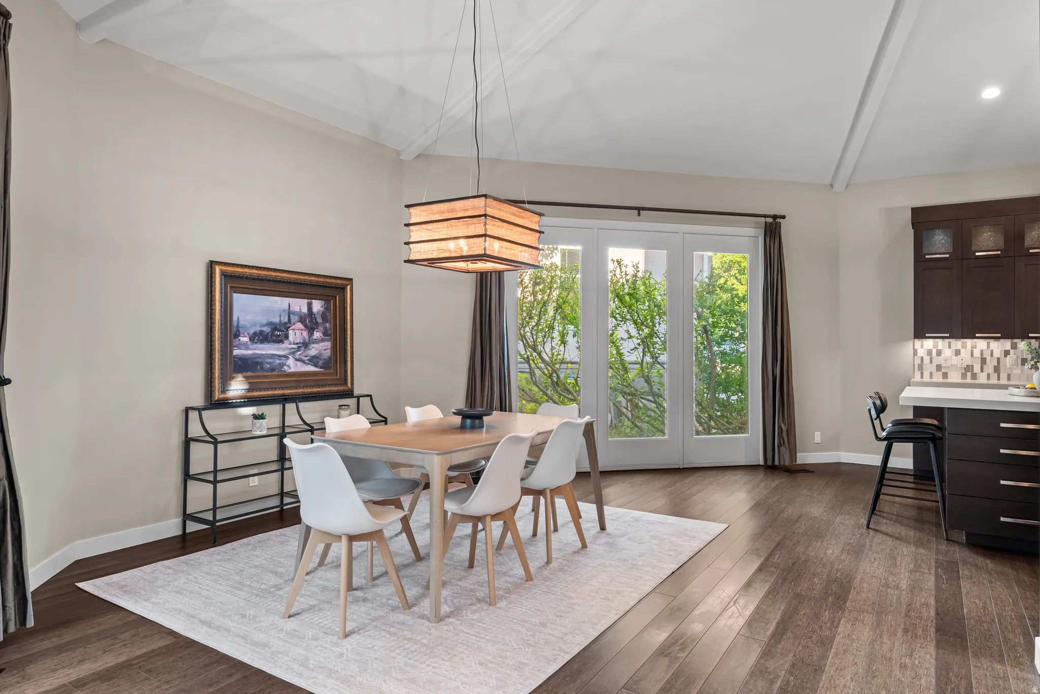 Dining area featuring a vaulted ceiling with exposed beams, wood-finish flooring, and a contemporary chandelier