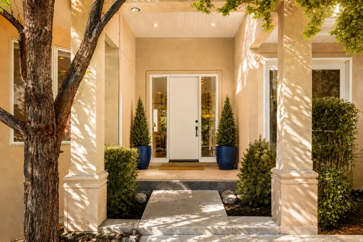 Covered entryway featuring a single white door with sidelights, stucco exterior, recessed lighting, concrete walkway, and established landscaping