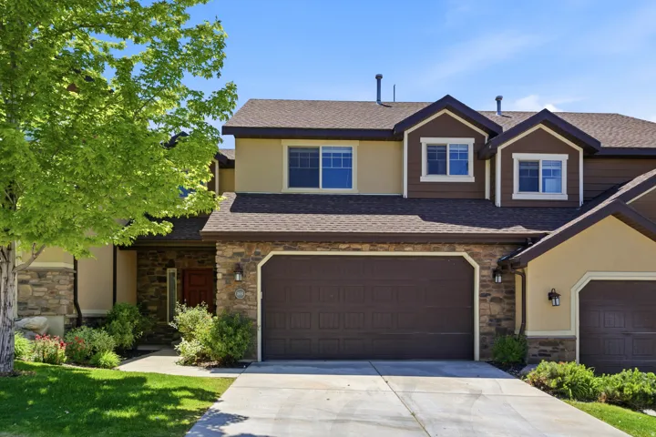 Multi-level residence featuring a stone facade, stucco siding, and a prominent two-car garage
