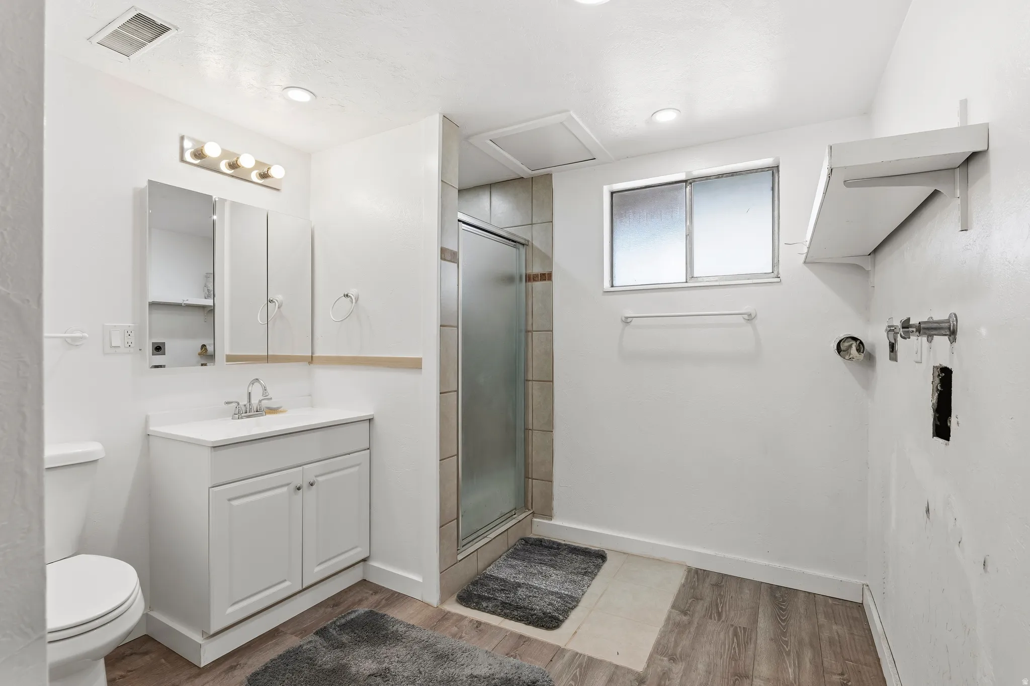 Bathroom featuring a white vanity with a single sink, a mirrored medicine cabinet, a glass-enclosed shower, and wood-finish flooring