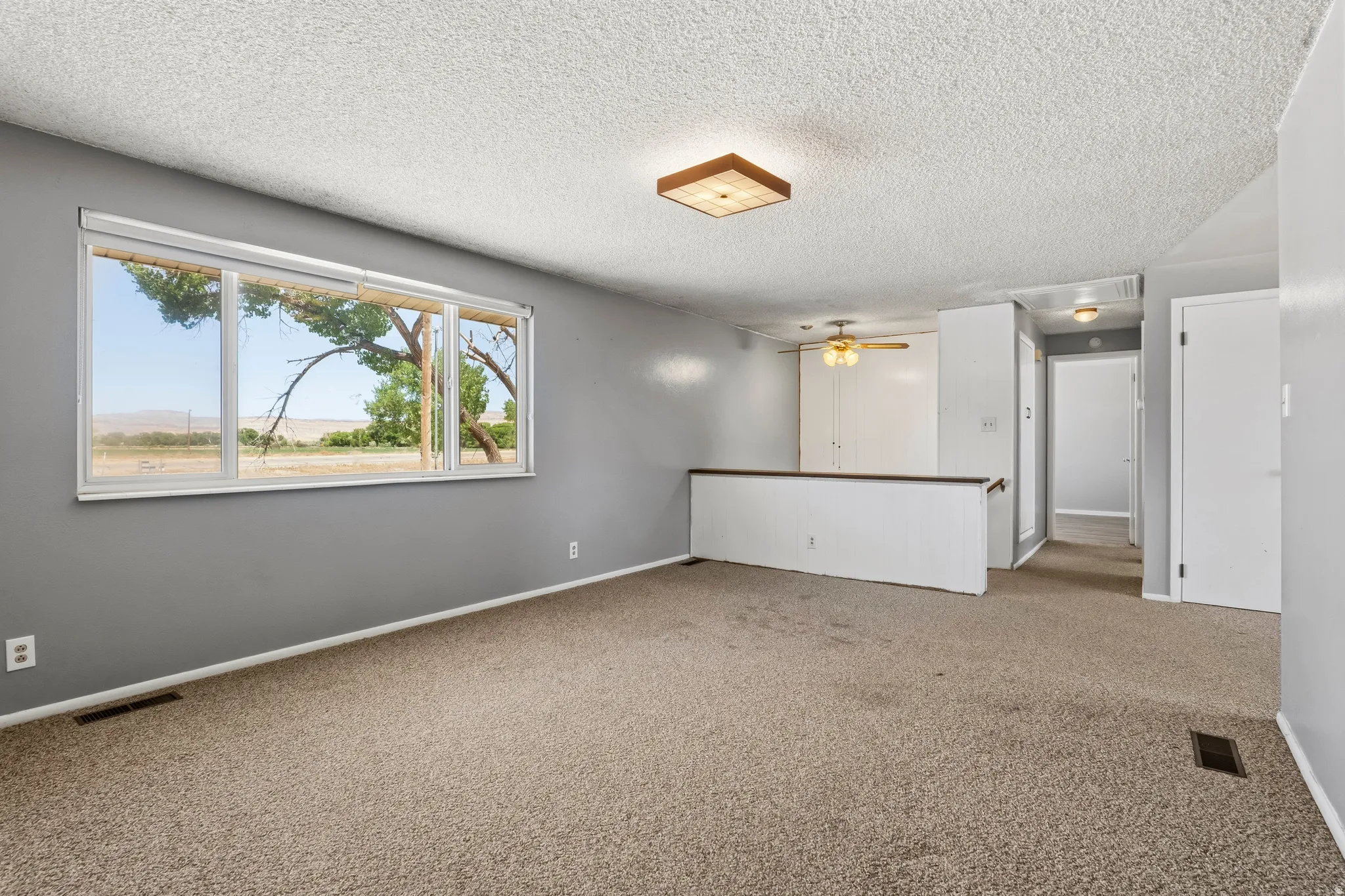 Carpeted living space featuring a large picture window, painted interior walls, and textured ceilings