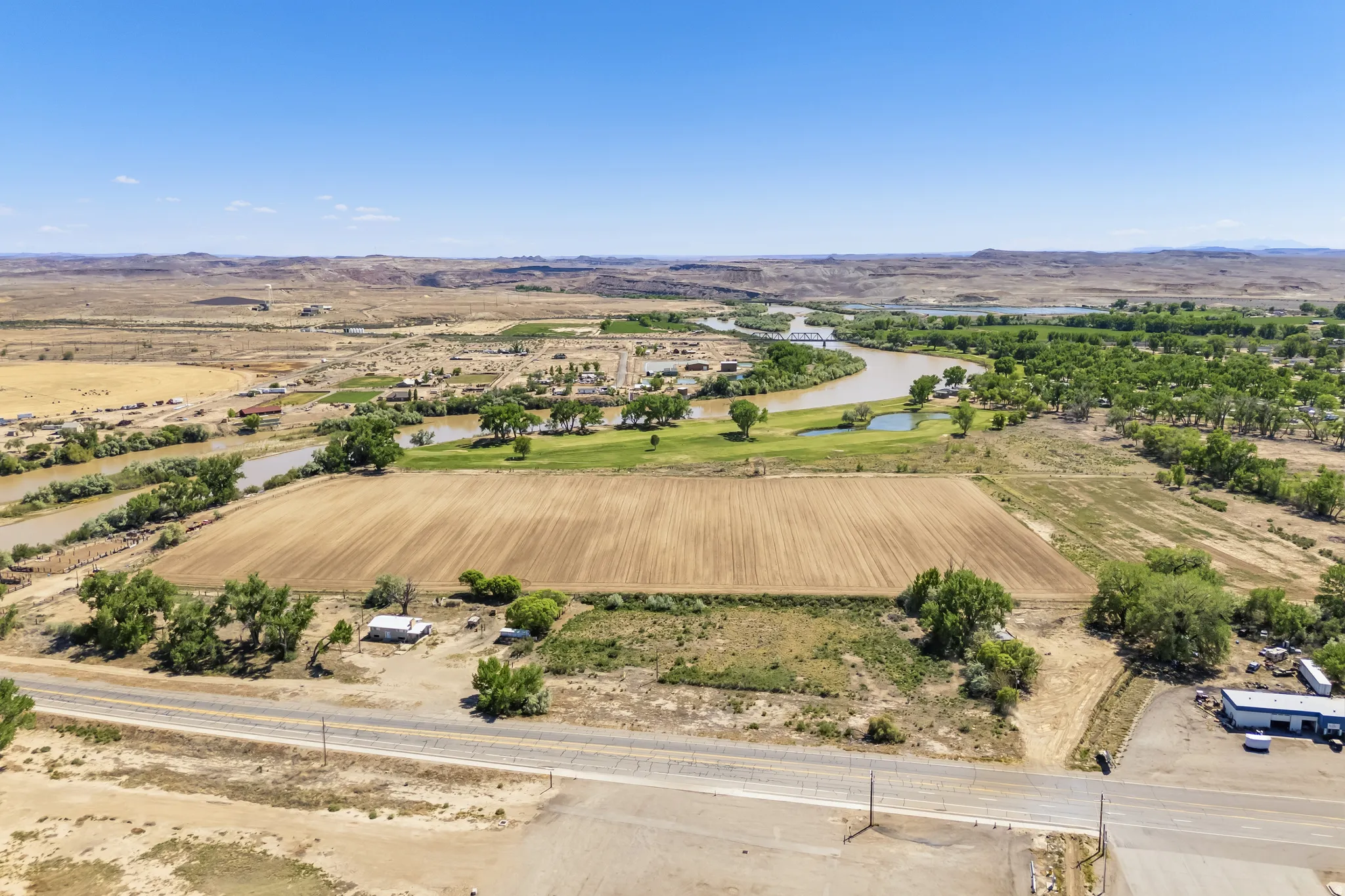 Expansive undeveloped land featuring a cleared field, surrounded by sparse vegetation and mature trees