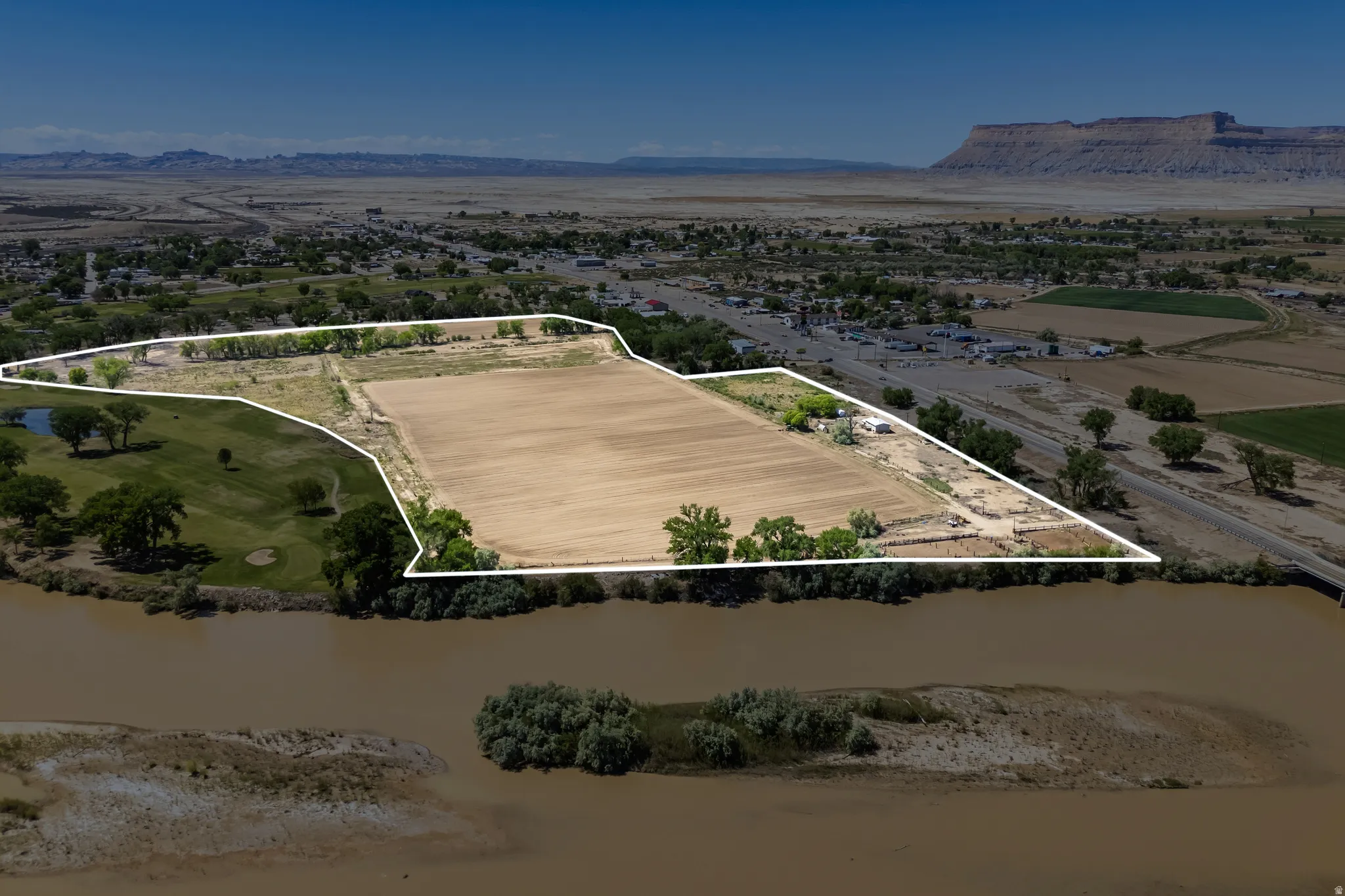 Expansive land parcel featuring a riverfront boundary, adjacent golf course, and a level, cleared field