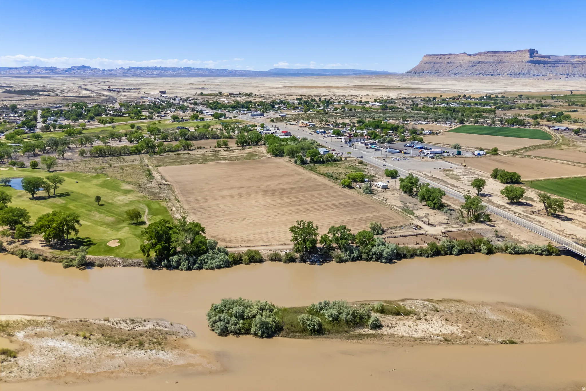 Expansive land parcel with river frontage, bordered by a golf course, agricultural fields, and a distant mesa backdrop