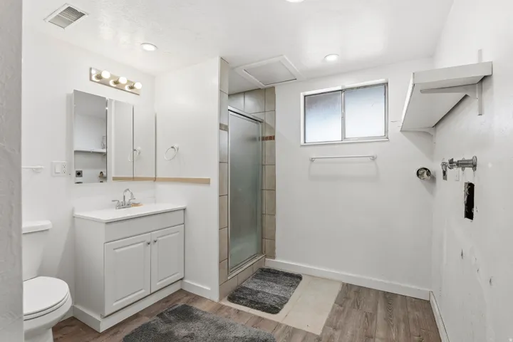 Bathroom featuring a white vanity with a single sink, a mirrored medicine cabinet, a glass-enclosed shower, and wood-finish flooring