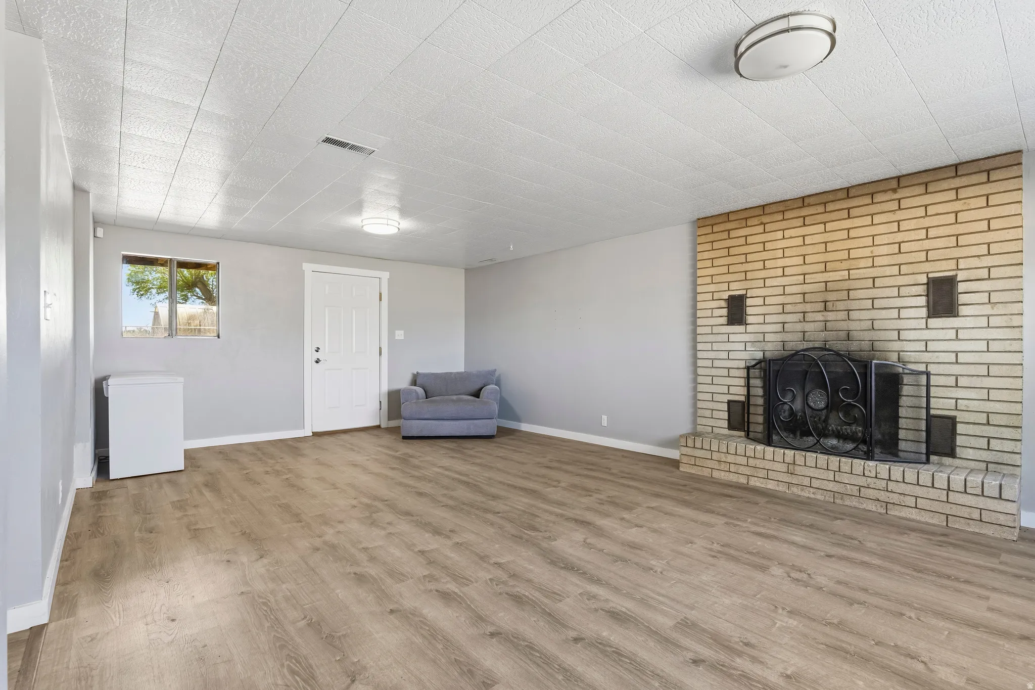 Living area featuring a brick fireplace with a black metal screen, wood-finish flooring, light grey walls, white trim, and two flush-mount ceiling lights
