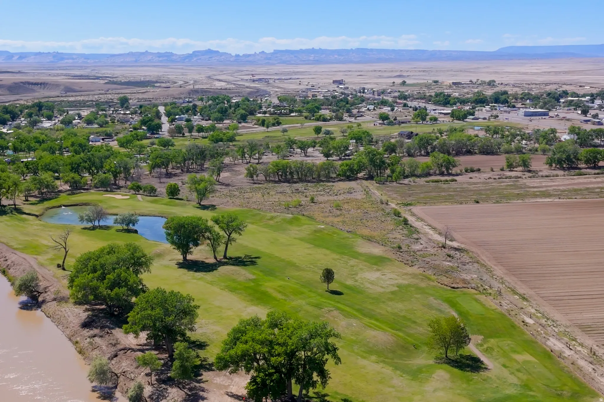Expansive green golf course featuring a water hazard, mature trees, and a bordering river