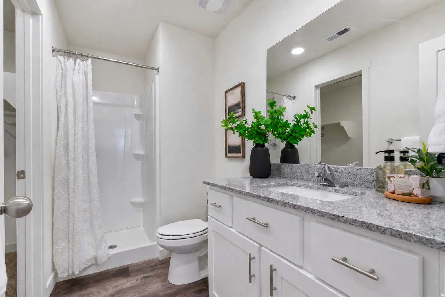 Bathroom featuring a white shower stall with built-in shelving, a white toilet, and wood-finish flooring