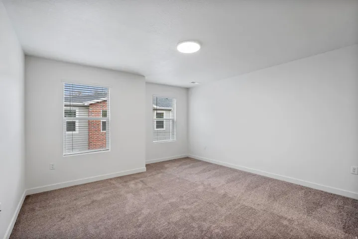 Neutral tone carpeting in a room featuring two windows with horizontal blinds and a ceiling-mounted light fixture