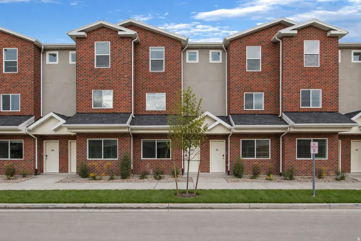 Modern townhome exterior featuring brick facade, multiple large windows, a covered entryway, and a shingle roof
