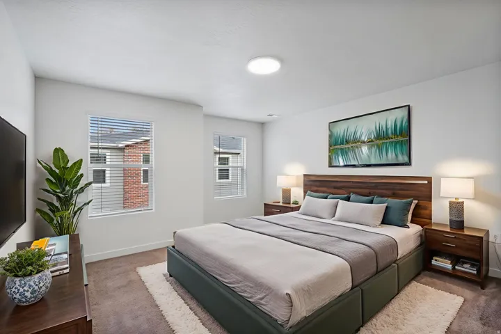 Carpeted bedroom featuring multiple windows with blinds, a built-in ceiling light fixture, and a wood-finish headboard