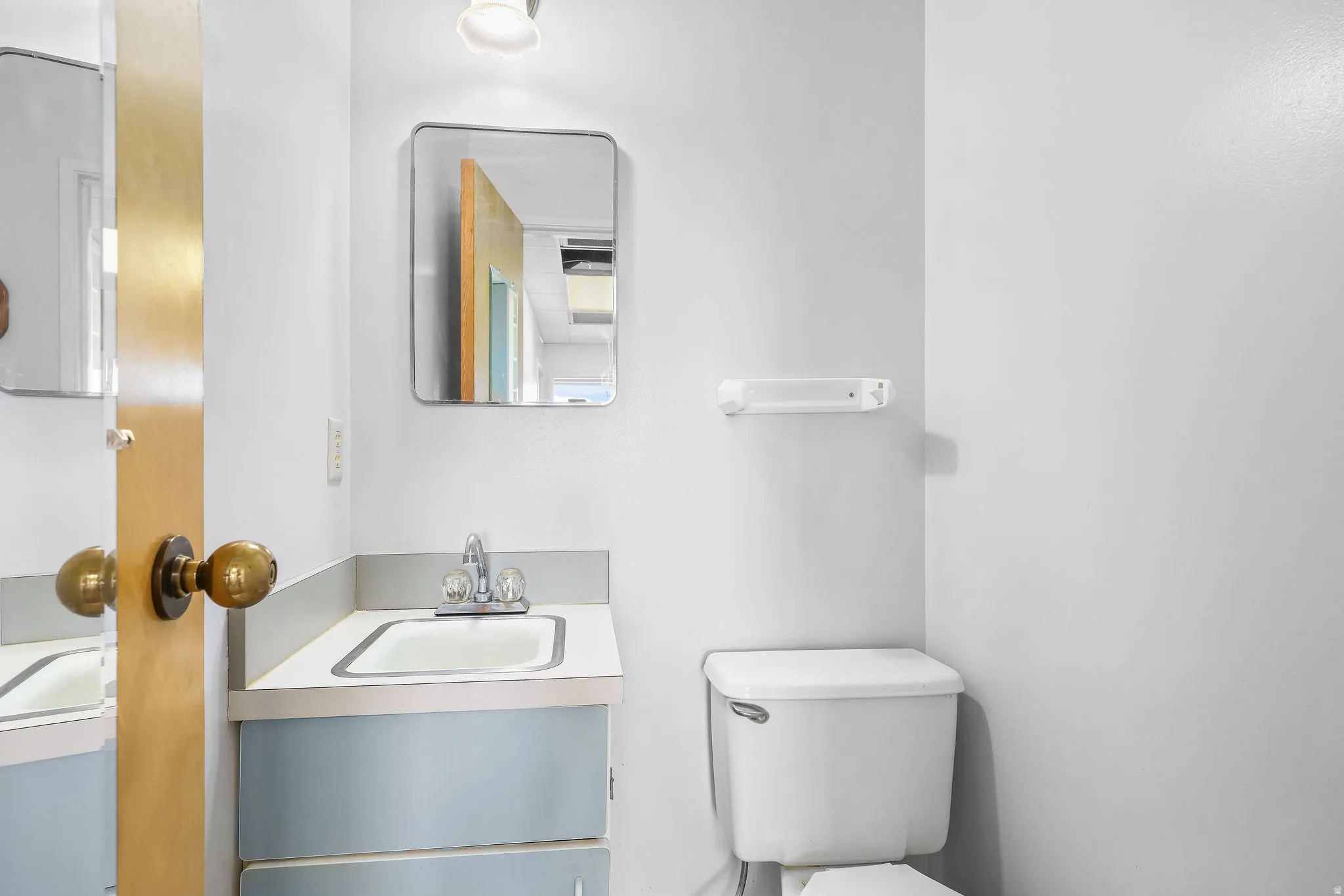 Bathroom featuring a light blue vanity with a laminate countertop, an integrated sink with chrome fixtures, a wall-mounted mirror, and a white toilet