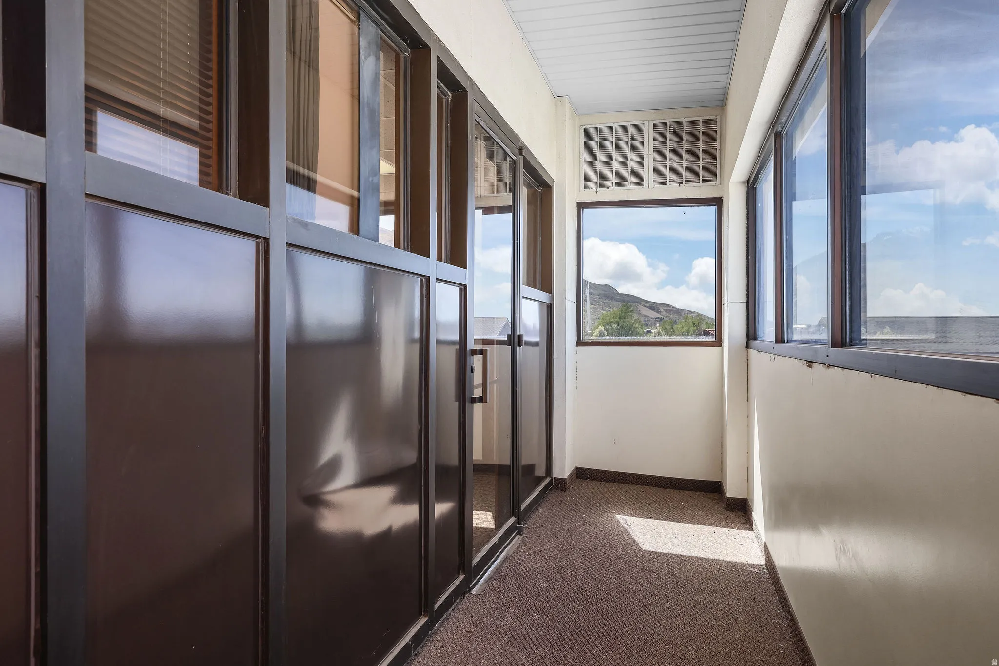 Enclosed balcony featuring expansive windows, mountain scenery, and carpet flooring