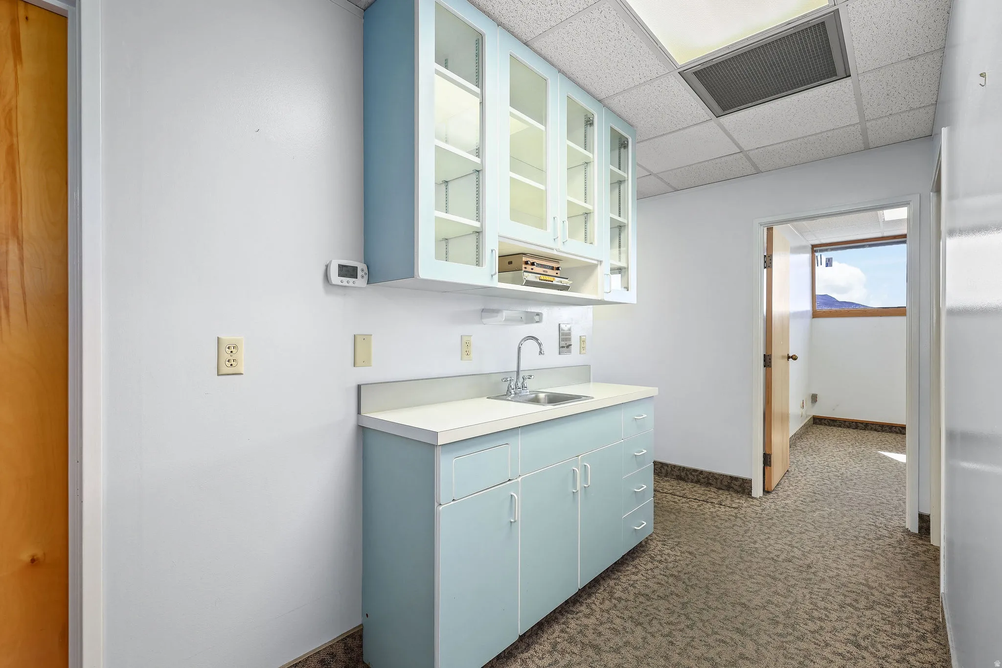 Light blue cabinetry with glass-front upper cabinets, a stainless steel sink, and a white countertop