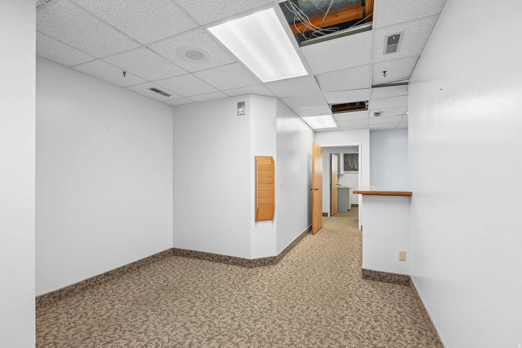 Commercial interior featuring patterned carpet flooring, white painted walls, and a dropped acoustic tile ceiling with fluorescent lighting
