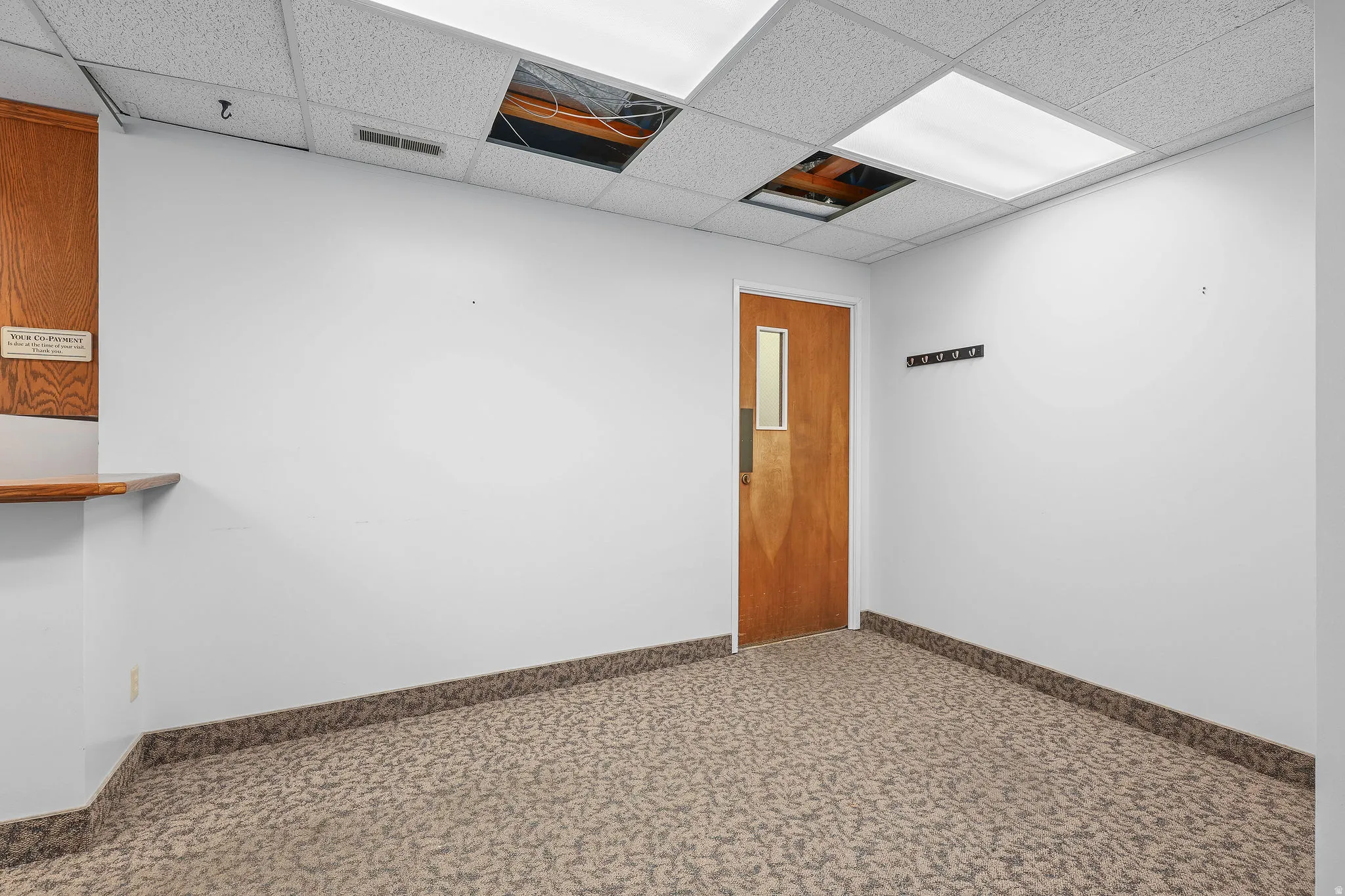 Interior room featuring patterned carpet flooring, white walls, and a drop ceiling with integrated lighting