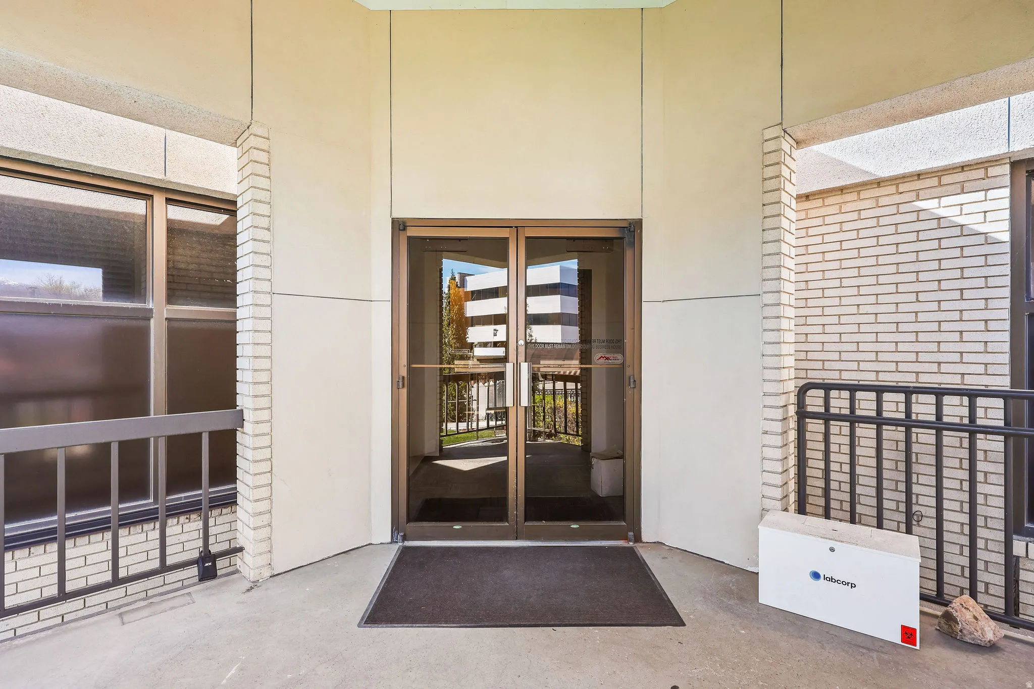 Building entrance featuring double glass doors, light brick facade, and concrete flooring