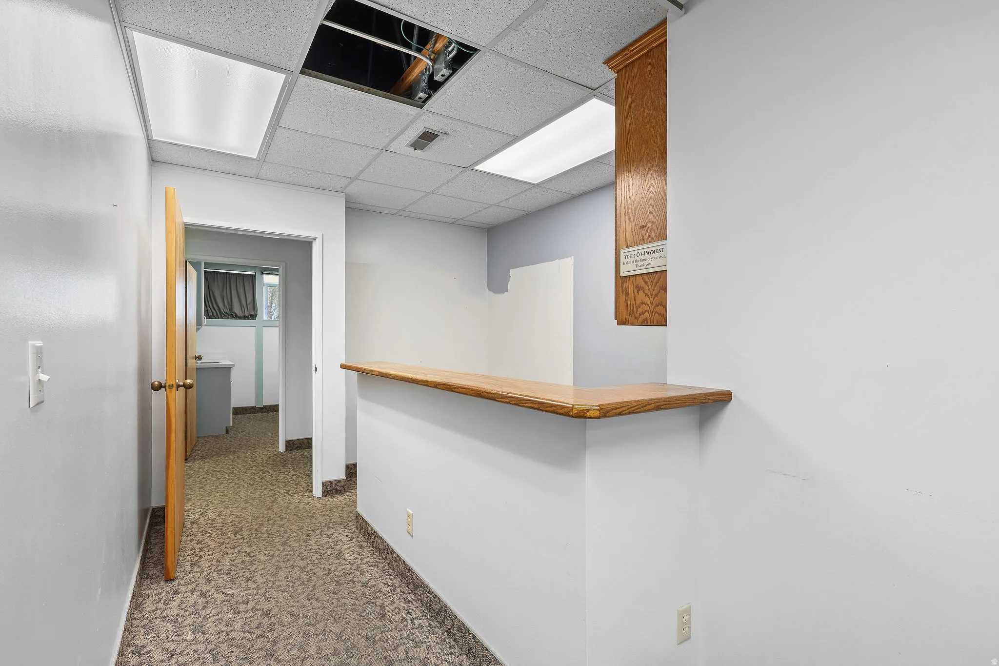 Reception area featuring a wood-finish counter, dropped ceiling with integrated lighting, and patterned carpet flooring
