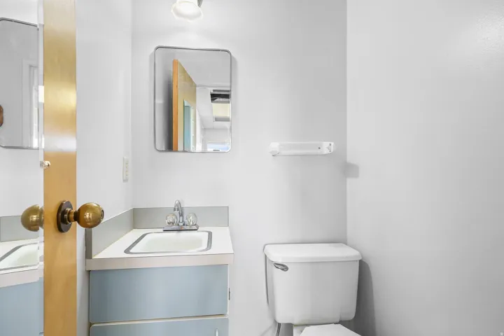 Bathroom featuring a light blue vanity with a laminate countertop, an integrated sink with chrome fixtures, a wall-mounted mirror, and a white toilet