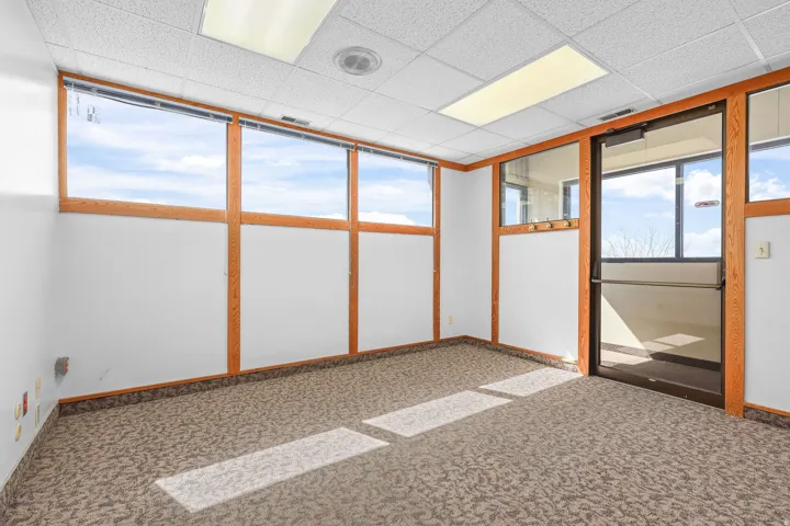 Commercial space featuring expansive window-lined walls, a drop ceiling with integrated lighting, patterned carpet flooring, and a glass-paneled entry door with a push bar