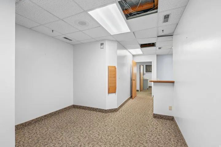 Commercial interior featuring patterned carpet flooring, white painted walls, and a dropped acoustic tile ceiling with fluorescent lighting