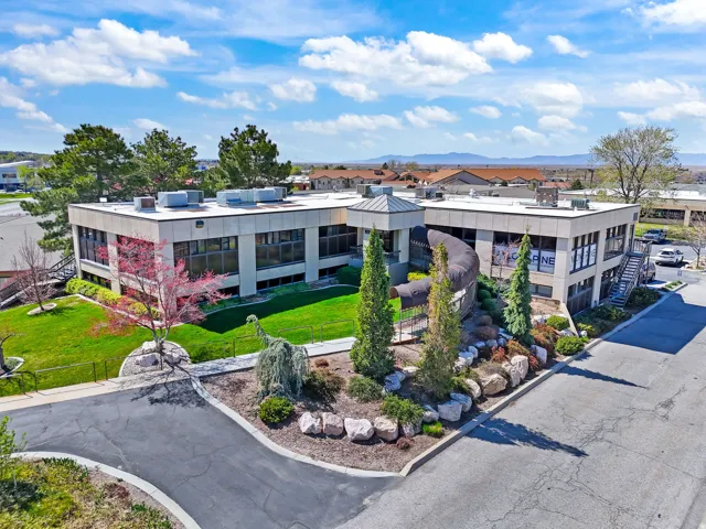 Two-story commercial building featuring extensive landscaping, an asphalt driveway, and a stone facade