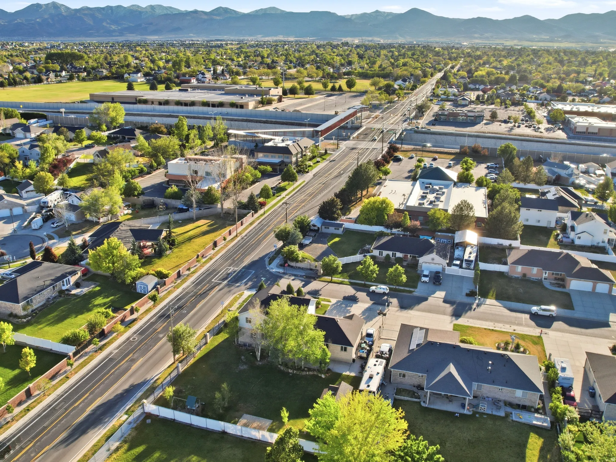 Aerial perspective showcasing a residential area with varied housing styles, mature trees, and mountainous backdrops